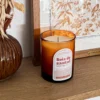 Bougie parfumée bois de santal en verre ambré, posée sur une étagère en bois dans une décoration naturelle et chaleureuse.