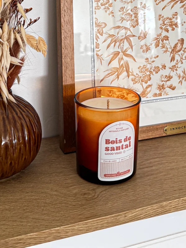 Bougie parfumée bois de santal en verre ambré, posée sur une étagère en bois dans une décoration naturelle et chaleureuse.