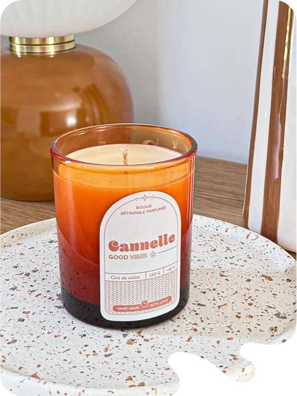 Bougie parfumée cannelle en verre ambré, posée sur un plateau en céramique dans un intérieur chaleureux.