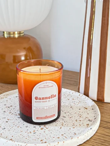 Bougie parfumée cannelle en verre ambré, posée sur un plateau en céramique dans un intérieur chaleureux.
