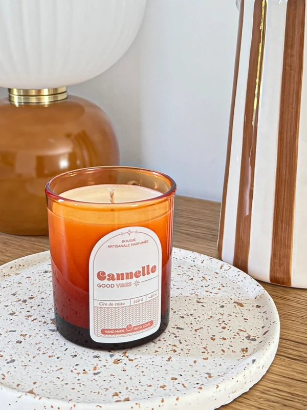 Bougie parfumée cannelle en verre ambré, posée sur un plateau en céramique dans un intérieur chaleureux.
