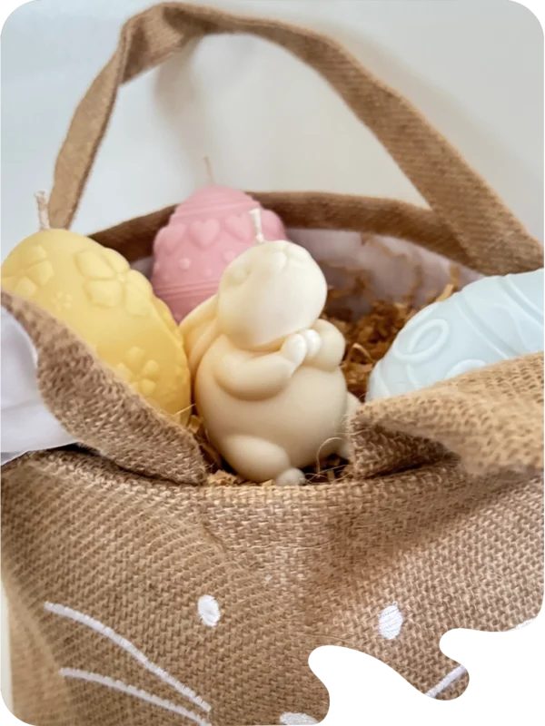 Panier en toile de jute en forme de lapin contenant des bougies artisanales en forme d’œufs et de lapin. Idée cadeau originale pour Pâques.