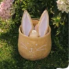 Panier décoratif en forme de lapin en tissu beige avec oreilles roses, ambiance printanière fleurie.