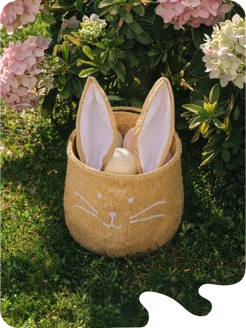 Panier décoratif en forme de lapin en tissu beige avec oreilles roses, ambiance printanière fleurie.