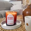 Bougie parfumée Crème Brûlée en verre ambré posée sur un plateau blanc, ambiance intérieure cosy avec vase décoratif et tasse sur une table en fibres naturelles.