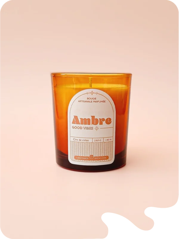 Bougie artisanale parfumée Ambre dans un verre ambré, sur fond rose. Une touche orientale et chaleureuse pour un intérieur cosy.