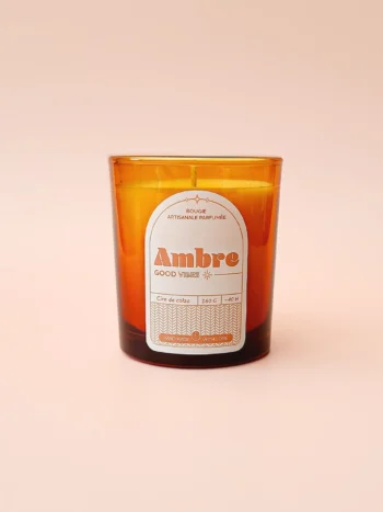 Bougie artisanale parfumée Ambre dans un verre ambré, sur fond rose. Une touche orientale et chaleureuse pour un intérieur cosy.