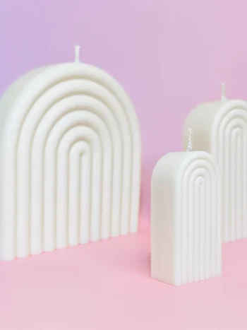 Ensemble de bougies artisanales en forme d’arche, blanches, sur fond rose et violet, créant une ambiance moderne et apaisante.