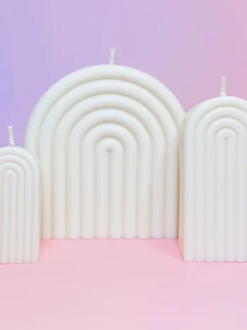 Trio de bougies Happy Arche en cire naturelle, design moderne en forme d’arche, sur fond rose et violet pour une décoration élégante et minimaliste.
