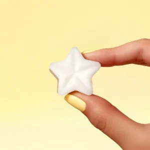 Fondant parfumé en forme d’étoile, parfum crème brûlée, tenu entre deux doigts avec vernis jaune, sur fond jaune pastel