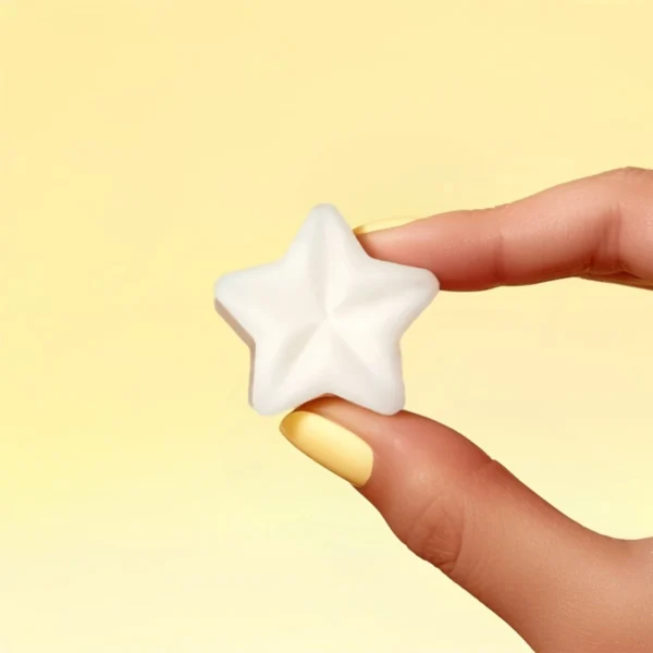 Fondant parfumé en forme d’étoile, parfum crème brûlée, tenu entre deux doigts avec vernis jaune, sur fond jaune pastel
