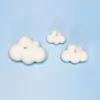 Trio de bougies décoratives en forme de nuage, fabriquées en cire végétale naturelle, posées sur un fond bleu ciel.