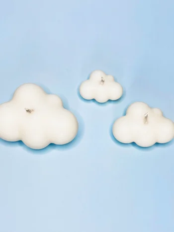 Trio de bougies décoratives en forme de nuage, fabriquées en cire végétale naturelle, posées sur un fond bleu ciel.