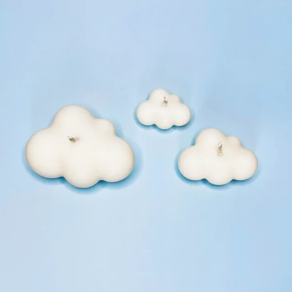 Trio de bougies décoratives en forme de nuage, fabriquées en cire végétale naturelle, posées sur un fond bleu ciel.
