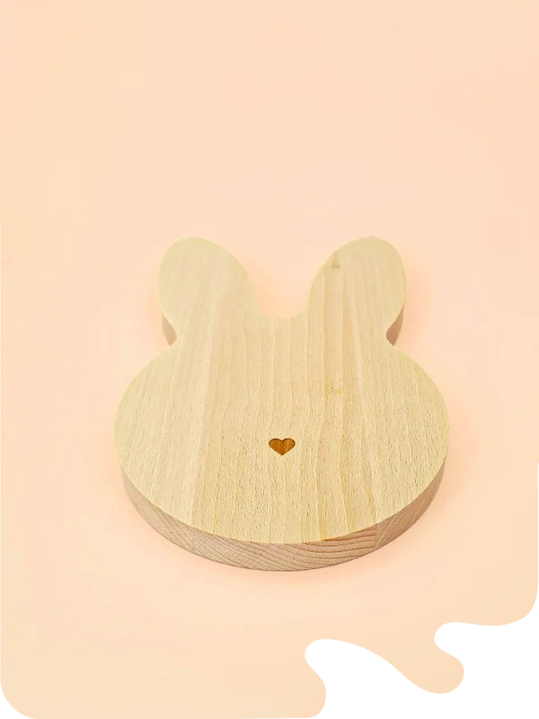 Support en bois naturel en forme de tête de lapin avec petit cœur gravé, conçu pour accueillir bougies décoratives, fondants ou accessoires déco, sur fond pastel.