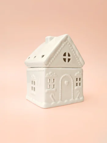 Brûle-parfum Sugar House - Maison en céramique pour fondants parfumés | Crème Brûlée Bougies Brûle-parfum Sugar House en céramique blanche, design maison de pain d’épices, vue de trois-quarts sur fond rose.