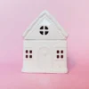 Brûle-parfum Sugar House en céramique blanche, vue de face avec détails sculptés et fenêtres ajourées, sur fond rose.