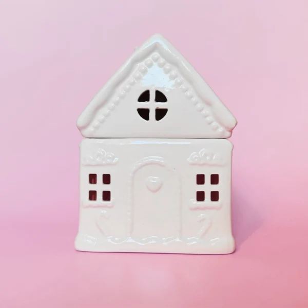 Brûle-parfum Sugar House en céramique blanche, vue de face avec détails sculptés et fenêtres ajourées, sur fond rose.