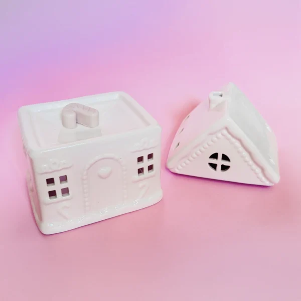 Brûle-parfum Sugar House en céramique blanche, en forme de maison avec toit amovible, sur fond rose pastel.
