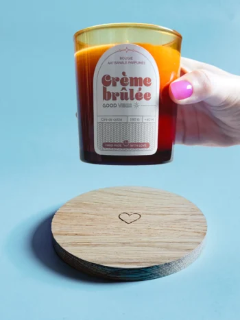 Support en bois gravé d’un cœur avec une bougie parfumée Crème Brûlée en cire de colza, ambiance chaleureuse et artisanale.