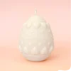 Bougie décorative en forme d’œuf avec motifs cœurs et reliefs, en cire naturelle, présentée sur fond pastel.