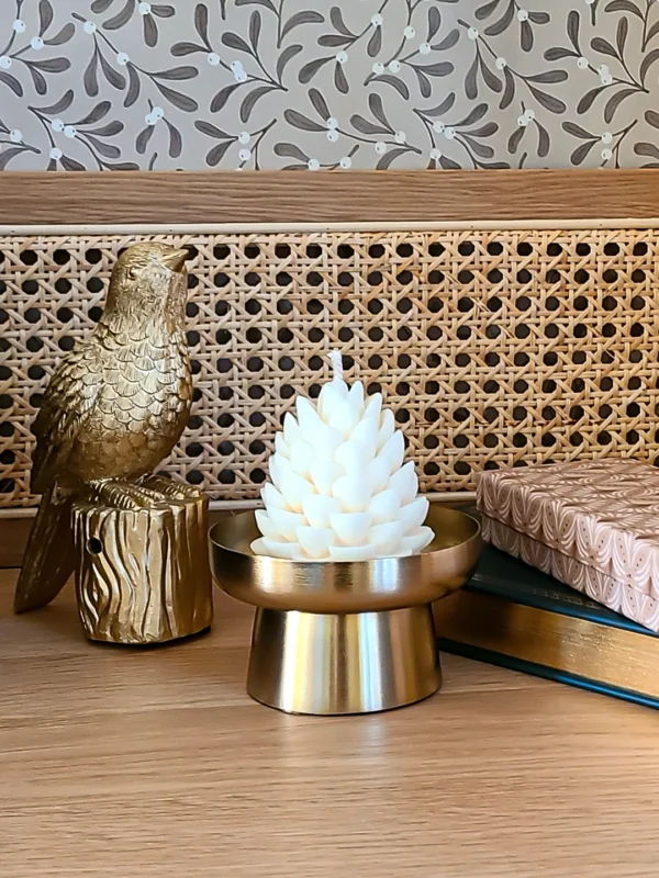 Bougie décorative Pompom Pinewood en forme de pomme de pin, création artisanale Crème Brûlée, présentée dans une déco dorée de Noël.