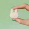 Fondant parfumé en forme de tête de lapin blanc, tenu entre deux doigts avec vernis vert pastel, sur fond vert, parfum printanier