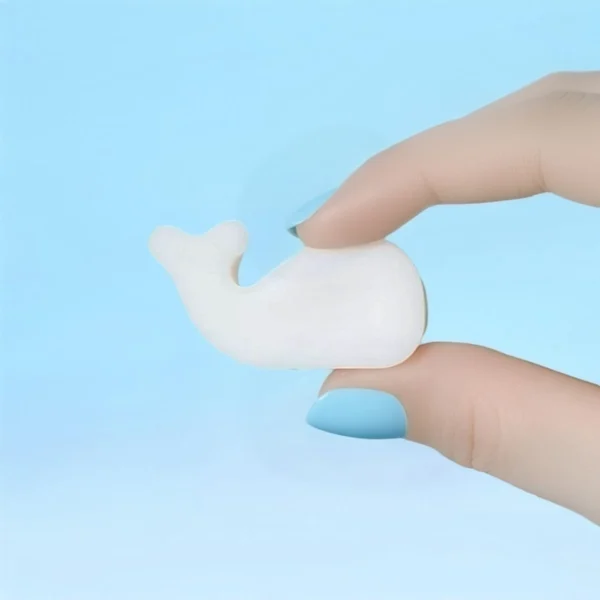 Fondant parfumé en forme de baleine tenu entre deux doigts avec vernis bleu, sur fond bleu pastel.