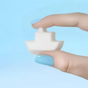 Fondant parfumé en forme de bateau tenu entre deux doigts vernis bleu, sur fond bleu pastel.