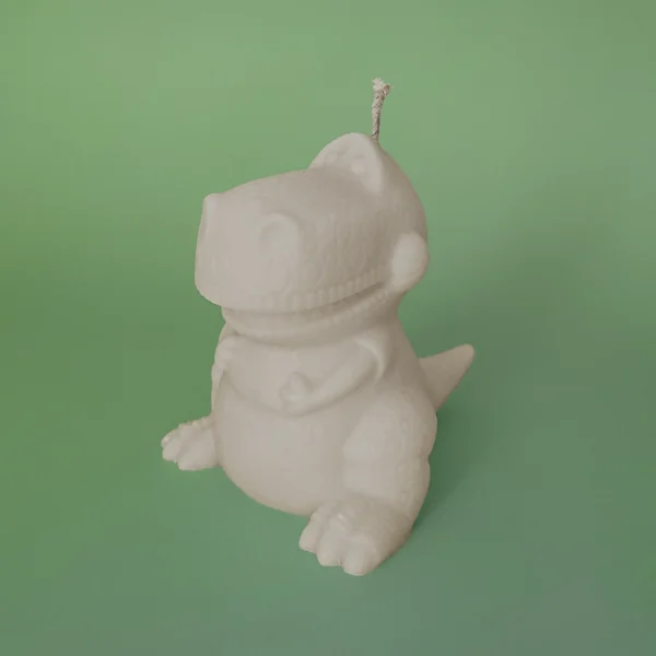 Bougie blanche en forme de dinosaure T-Rex rigolo posée sur fond vert pastel.