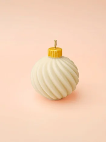 Bougie décorative Bubble Glow en cire naturelle, forme boule torsadée avec capuchon doré, présentée sur fond rose pastel.