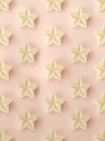 Fondants parfumés Crème Brûlée en forme d’étoile, présentés en motif répétitif sur un fond rose pastel.