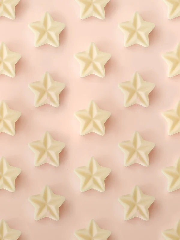 Fondants parfumés Crème Brûlée en forme d’étoile, présentés en motif répétitif sur un fond rose pastel.