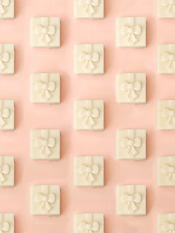 Fondants Fiery Gift | Feu de bois Fondants parfumés Fiery Gift en forme de petit cadeau, parfum feu de bois, présentés en motif répétitif sur un fond rose pastel.