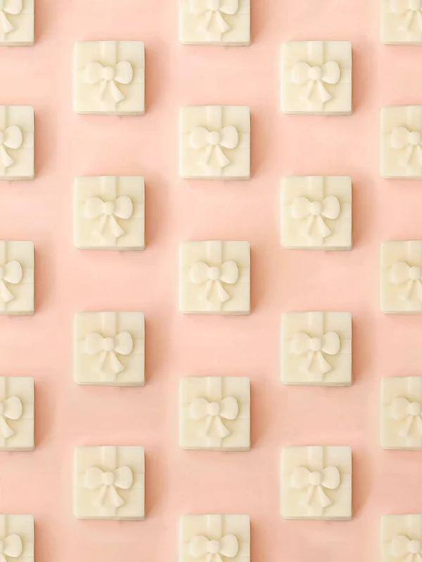 Fondants parfumés Fiery Gift en forme de petit cadeau, parfum feu de bois, présentés en motif répétitif sur un fond rose pastel.