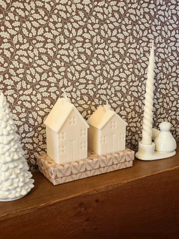 Bougies décoratives en forme de maison, présentées sur une étagère dans une ambiance de Noël naturelle et chaleureuse.