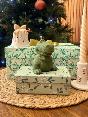 Bougie décorative verte en forme de dinosaure Roooaar, posée sur des boîtes cadeaux devant un sapin de Noël.