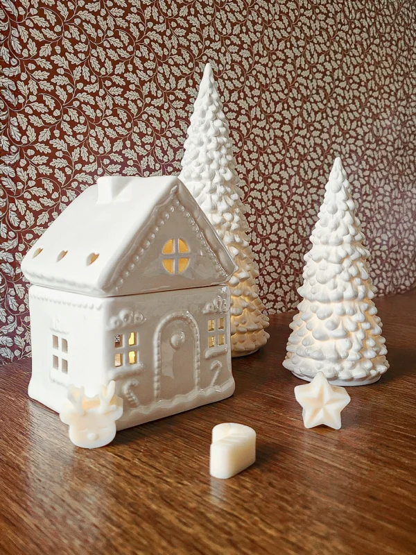 Brûle-parfum Sugar House en céramique blanche, présenté avec des sapins décoratifs dans une ambiance de Noël chaleureuse.