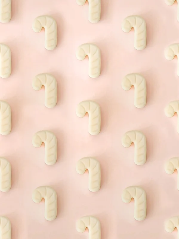 Fondants parfumés Sugar Rush en forme de sucre d’orge, parfum cannelle, présentés en motif répétitif sur un fond rose pastel.