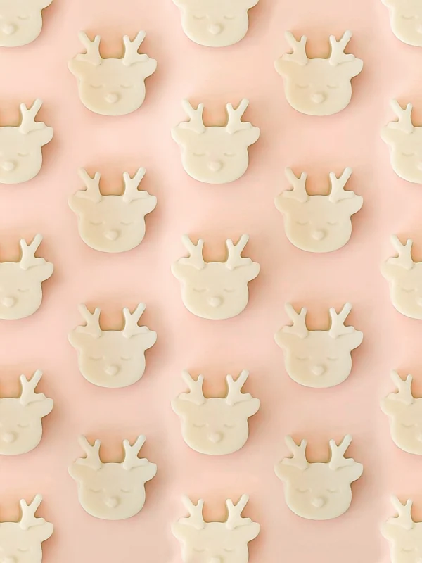 Fondants parfumés Wild Wild Melt en forme de tête de renne, parfum ambre, présentés en motif répétitif sur un fond rose pastel.