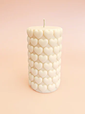 Bougie décorative Big Crush en cire naturelle, forme cylindrique ornée de cœurs en relief, couleur ivoire, présentée sur un fond pastel.