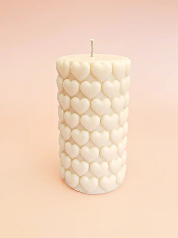 Bougie décorative Big Crush en cire naturelle, forme cylindrique ornée de cœurs en relief, couleur ivoire, présentée sur un fond pastel.