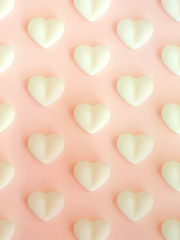 Fondant parfumé en forme de cœur à la rose et à la violette, en cire végétale de colza, présenté sur fond rose pastel.