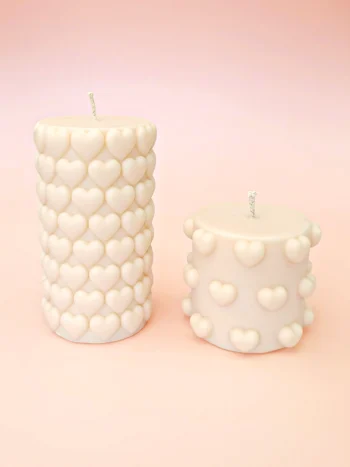 Bougies décoratives Double Crush en cire naturelle, deux formats cylindriques ornés de cœurs en relief, couleur ivoire, présentées sur un fond pastel.