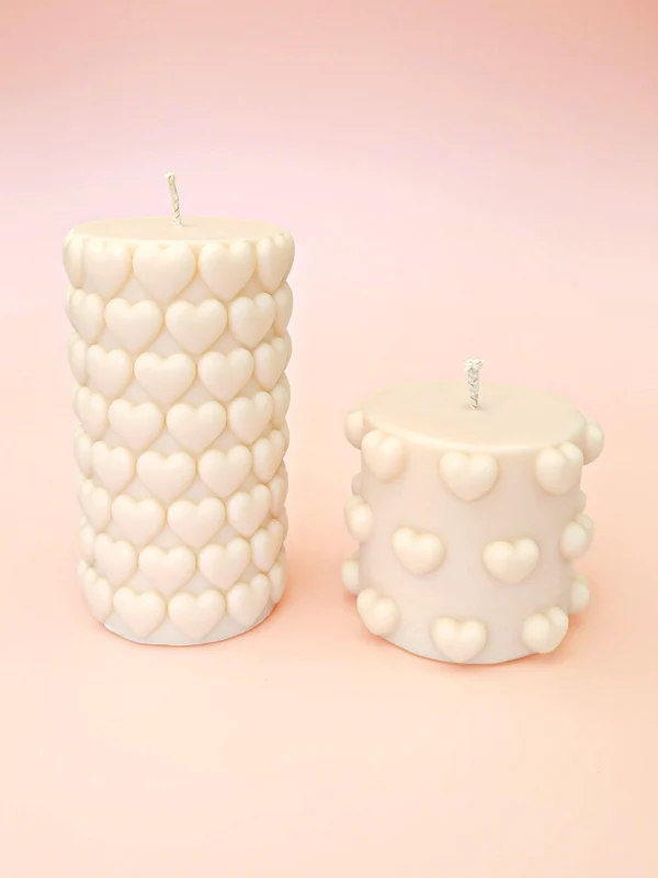Bougies décoratives Double Crush en cire naturelle, deux formats cylindriques ornés de cœurs en relief, couleur ivoire, présentées sur un fond pastel.