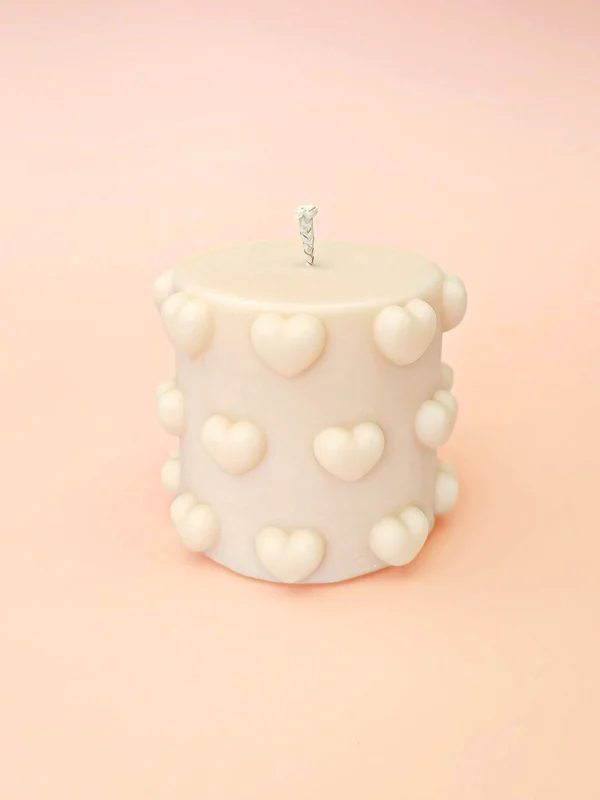 Bougie décorative Little Crush en cire naturelle, format cylindrique compact avec cœurs en relief, couleur ivoire, présentée sur fond pastel.